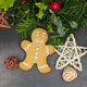 A gingerbread man cookies decorated with icing, next to a straw star and holly, on a grey surface.