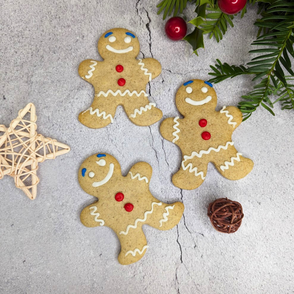  Three gingerbread men biscuits with white icing and red buttons on a table with Christmas decorations.