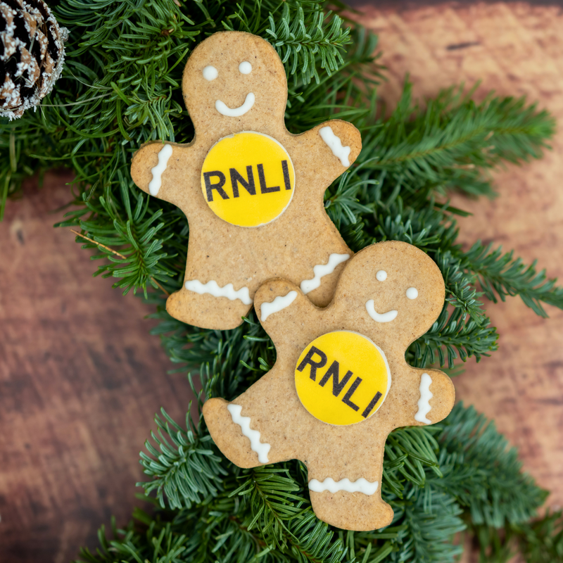 Two gingerbread men biscuits with RNLI logos, decorated with white icing and resting on festive greenery.