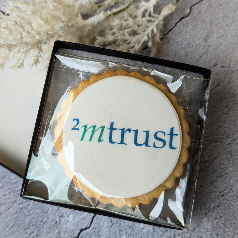 Company logo biscuit in a small box, featuring the "2mtrust" logo on a frosted cookie.