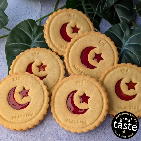 Six golden Eid Mubarak Celebration Biscuits with red star and crescent jam designs. Printed with "Eid Mubarak". Green leaves and Great Taste 2023 logo visible.