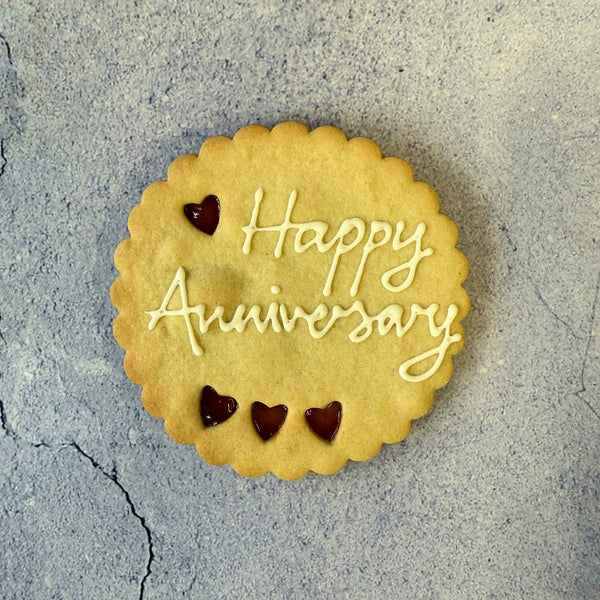 A round cookie with "Happy Anniversary" in icing and three heart-shaped jam cut-outs.