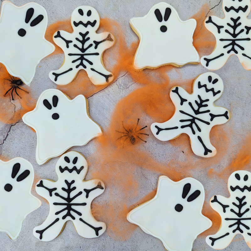 Iced Ghost & Skeleton Party Pack biscuits stuck on the spider's web. The biscuits are shaped like ghosts and Skeletons .
