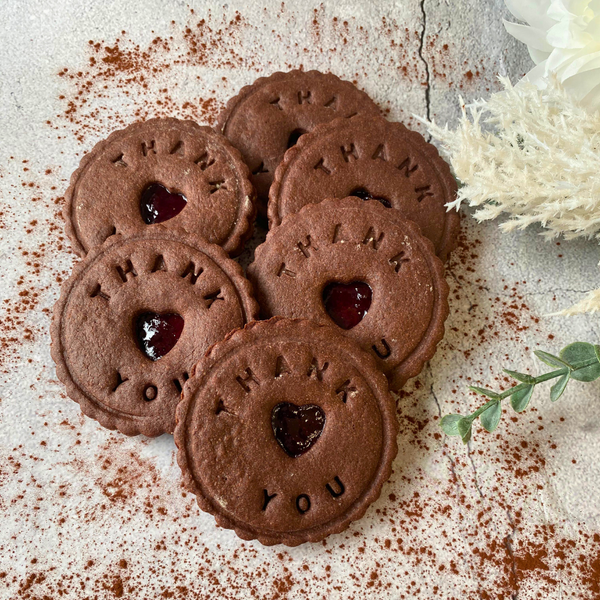 Stack of round chocolate digestive biscuits with heart-shaped centers filled with jam.