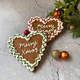 Two iced gingerbread heart biscuits with "Merry Xmas" message, red & green icing, & festive decorations. 