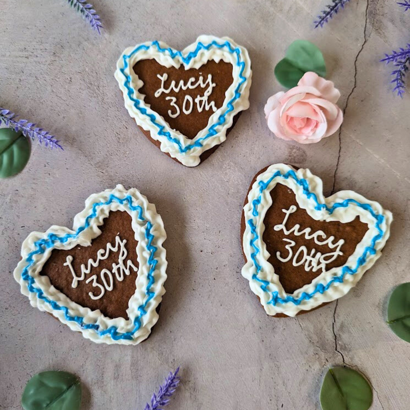 Three heart-shaped iced Oktoberfest cookies with "Lucy 30th" message, decorated with blue icing