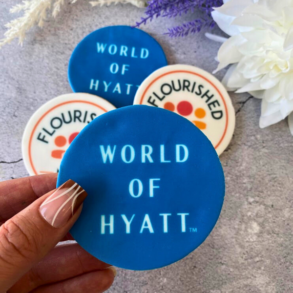  Hand holding a blue fondant biscuit printed with the "World of Hyatt" logo