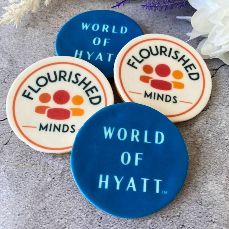 The round fondant biscuits printed with blue "World of Hyatt" and orange "Flourished Minds" logos.
