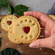 Hand holding a jam biscuit with "Thank You" message and heart-shaped cutout from staff or client appreciation gift box.