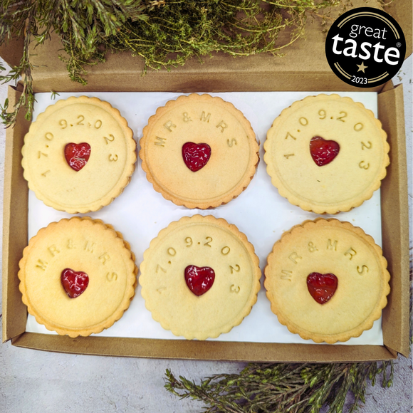 Box containing six Jam wedding biscuits, with heart-shaped biscuits at the centre, arranged on a table, adorned with a yellow ribbon for the MR&MRS couple 