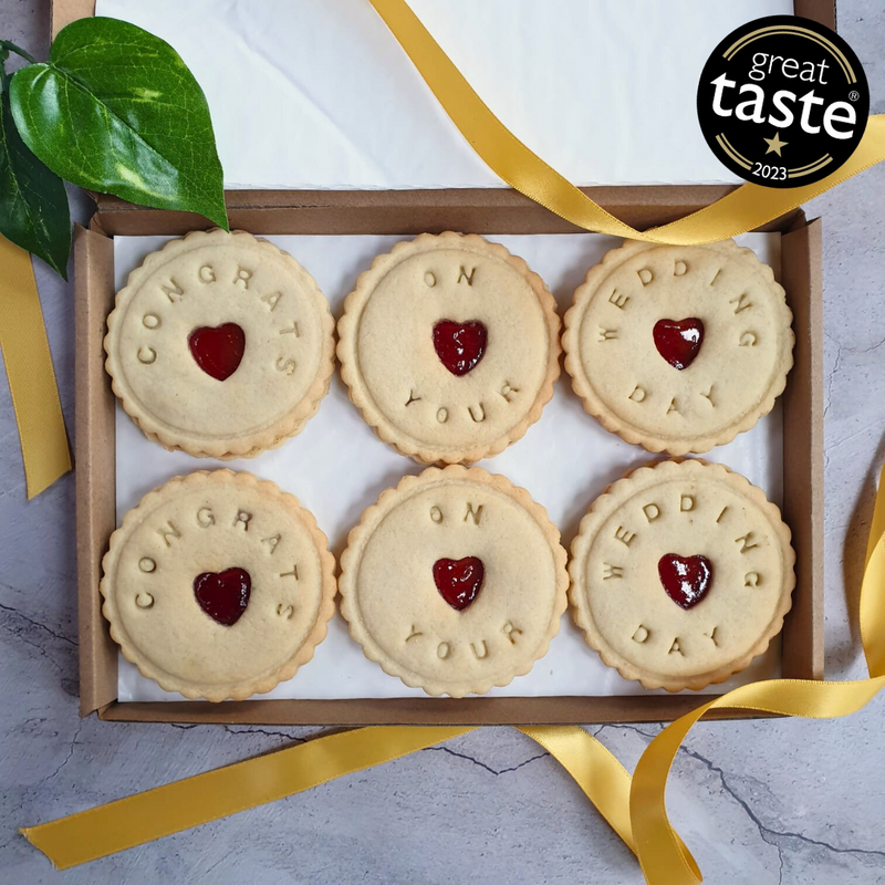 A box of six bespoke jam biscuits with heart-shaped cut-outs in the middle. The biscuits are decorated with the words 'Congratulations on your wedding!'