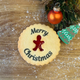 A golden jam biscuit with a red gingerbread-shaped centre is printed with "Merry Christmas". Festive decorations in the background