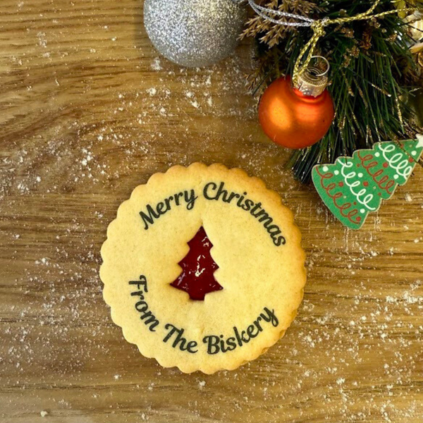 A golden jam biscuit with a red gingerbread-shaped centre is printed with "Merry Christmas from the Biskery". Festive decorations in the background