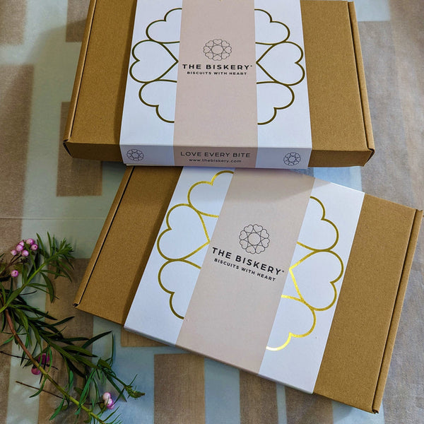 Boxes labelled 'The Biskery' and 'Love Every Bite' sit on a table, filled with Iced Happy Anniversary Biscuits